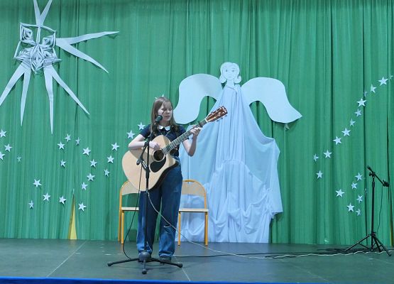 Uczennica klasy ósmej gra na gitarze i śpiewa kolędy